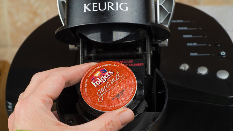 Keurig kahve makinesine koymak üzere olduğu kırmızı Folgers kahve kapsülünü tutan kişi.