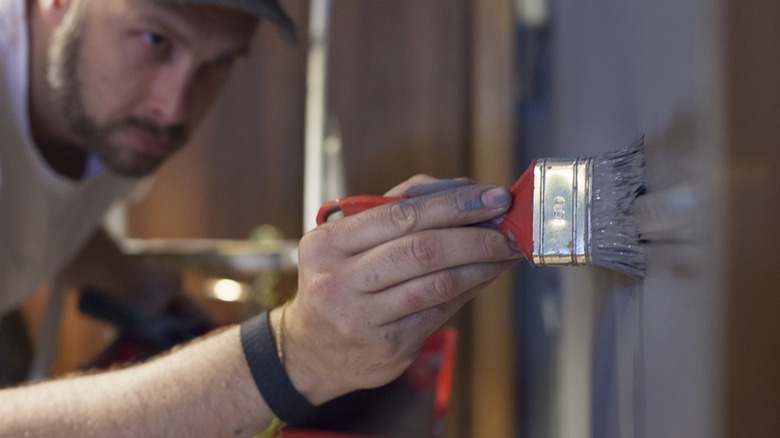 Duvara koyu renkli boya uygulamak için boya fırçası kullanan adam