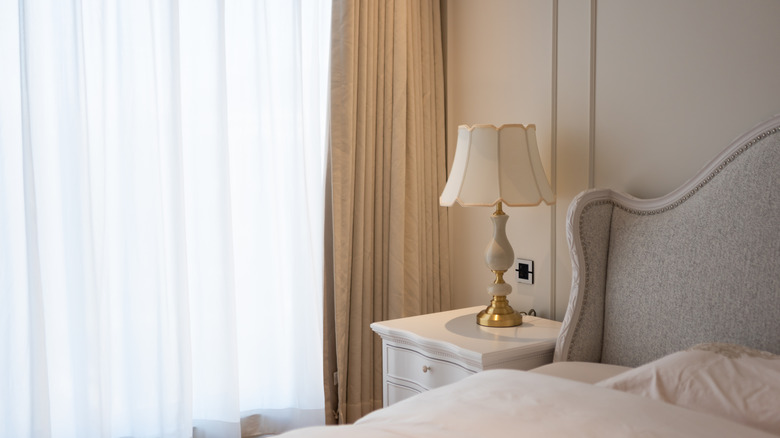 Beyaz ve altın kavisli bir başlık ve vintage tarzı lambayı ortaya çıkaran nötr temalı bir yatak odası.