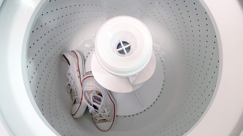 Bir çift kirli beyaz spor ayakkabı, su ile doldurulurken bir çamaşır makinesinin dibindedir