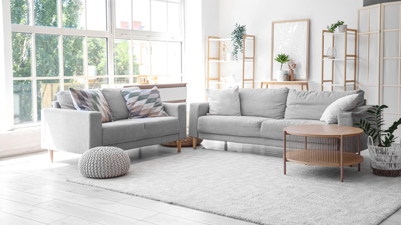 Büyük bir oturma odasında gri kanepe, halı ve peluş örgülü osmanlı