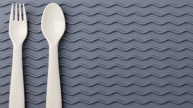 Plastik bir çatal ve kaşık gri bir silikon paspasın üzerine oturur.