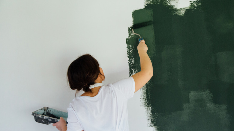 Bir duvarı koyu yeşil boyayan bir kişi.