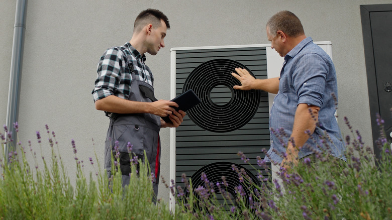 Bir teknisyen ve ev sahibi bir ısı pompasının yanında durur