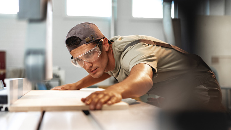 Bir masa testeresi ile odun bir levhayı kesen adam.