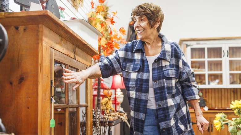Bir mağazada vintage mobilyaları inceleyen gülümseyen bir kıdemli kadın