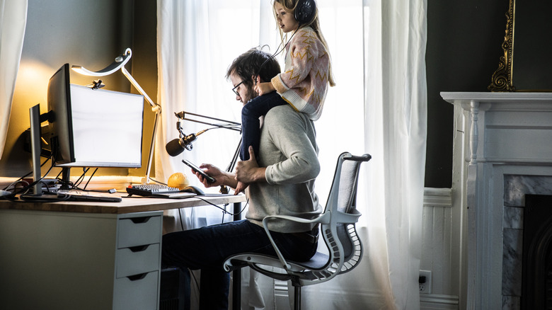 Bir adam telefonuna ev ofisinde küçük bir kızla bakıyor