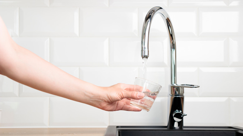 El, musluktan su ile doldurmak için bir bardak tutar
