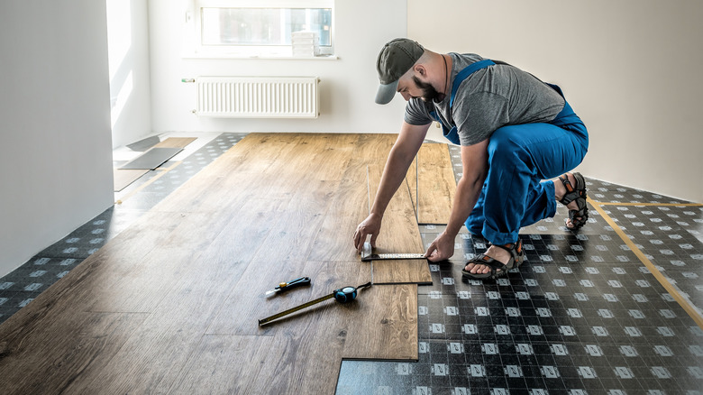 Gri kapak ve mavi tulumlu gömlek giyen bir profesyonel laminat döşeme takıyor