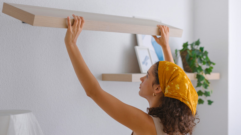Altın renkli bir kerchief'teki genç bir kadın kendi başına ahşap bir raf asıyor.