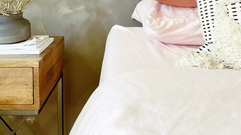 Pembe çarşaflı bir yatak odasında kireç yıkanmış bir duvar ve bir bitki