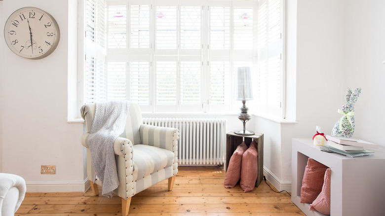 Büyük bir pencere penceresini kaplayan beyaz iç panjurlara sahip bir oturma alanı