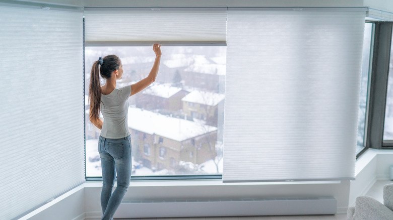 Büyük pencerenin önünde hücresel tonları kapatan kadın