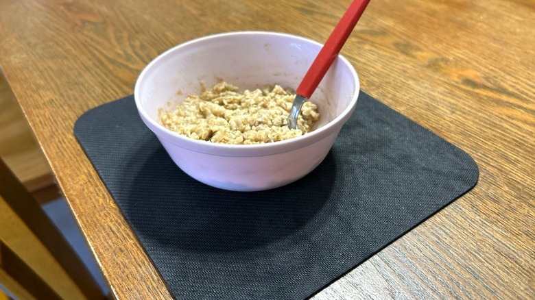 Ahşap yemek masasında mousepad üzerinde pembe plastik kasede hazırlanmış yulaf ezmesi