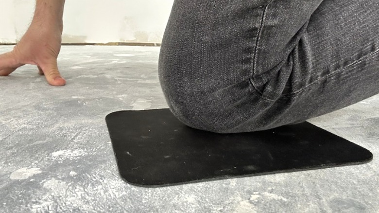 Beton zeminde diz çökerken mousepad üzerinde diz yastıklayan adam