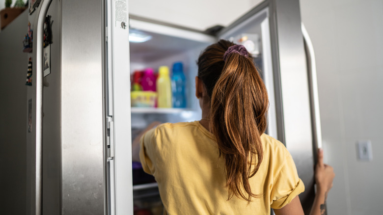 Yan yana dondurucu ve buzdolabı kapısı açık sarı bir gömlek giyen bir kız.