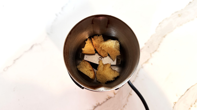 Mermer bir yüzeyde bir kahve değirmeni içinde küçük ekmek parçaları.