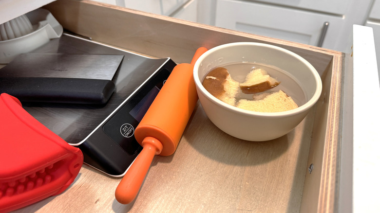 Ölçekli bir çekmecede küçük bir kase ekmek ve sirke, pim silindiri ve yanındaki diğer mutfak eşyaları.