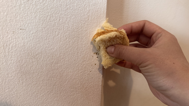 Üzerinde kahverengi izler bulunan bir duvara bir parça ekmek tutan eller.