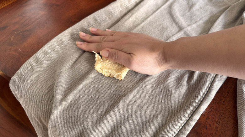 Bir parça ekmek parçasını lekeli kot üzerine bastırıyor.