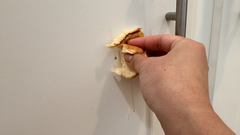 Beyaz mutfak dolabı kapısında lekelere bir parça ekmek tutan bir el.