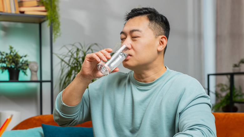 Bir bardak su içen yeşil bir sweatshirtli bir adam.