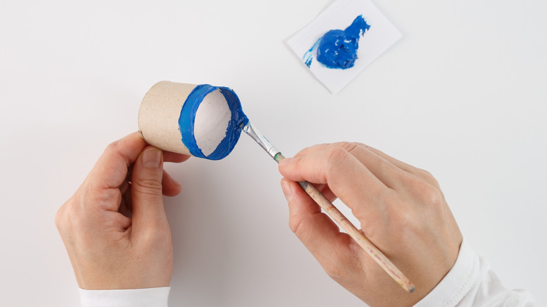 Bir kişi bir karton tuvalet kağıdı tüp mavisi boyuyor.