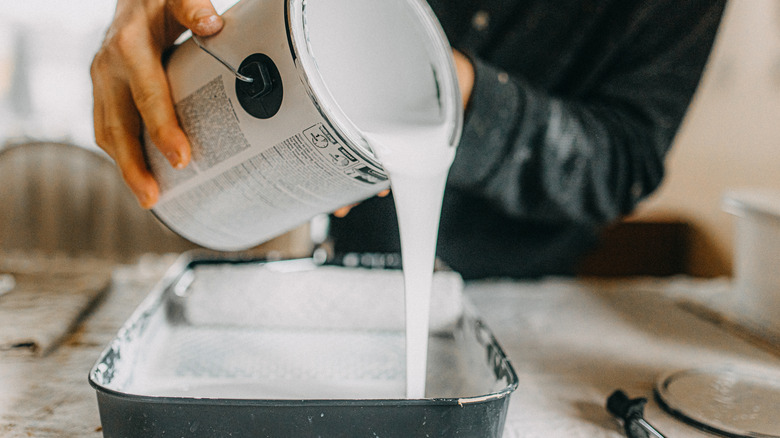 Gri bir tepsiye bir kutu beyaz boya döken siyah bir gömlek giyen bir adam