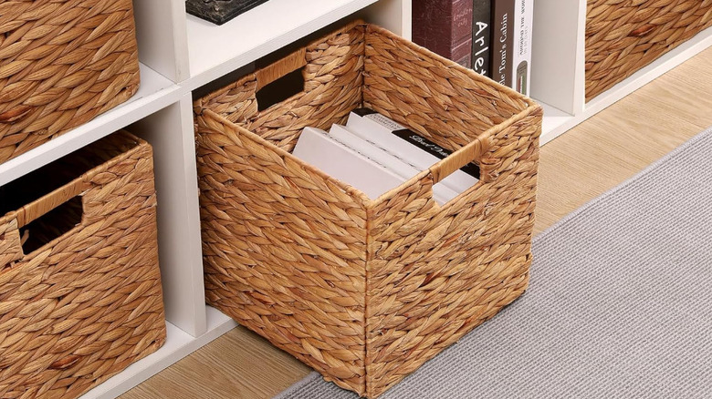 Kitaplarla dolu dokuma bir depolama küpü beyaz bir raftan çekilir.