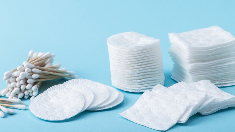 Pamuklu çubuklar, iki yığın dairesel pamuk turu ve hafif turkuaz arka plan üzerinde iki yığın kare pamuklu pedy dahil olmak üzere bir çeşit pamuklu ürün