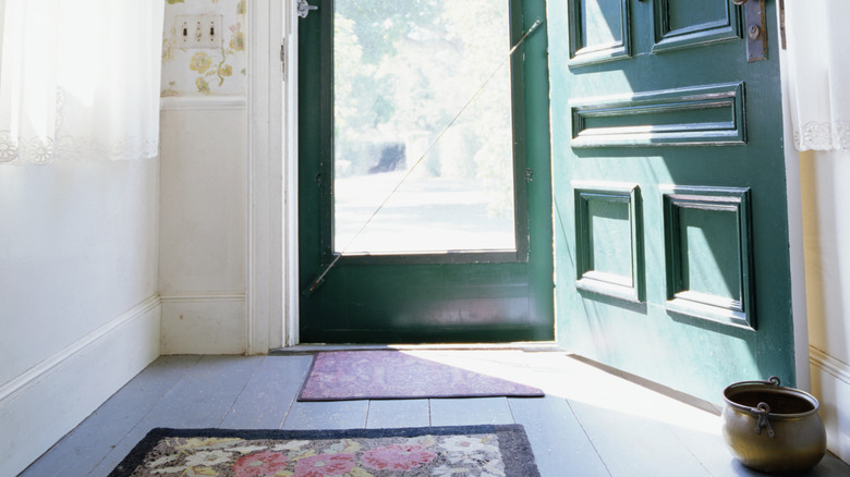 Açık bir ön kapının önünde zeminde bir paspas ve bir halı