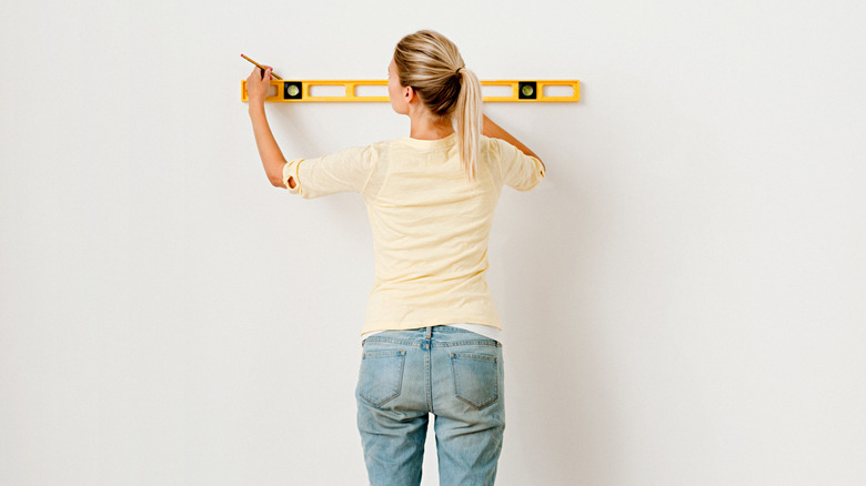 Fenülde beyaz bir duvara çizgi çizen bir ruh seviyesi tutan bir kadın