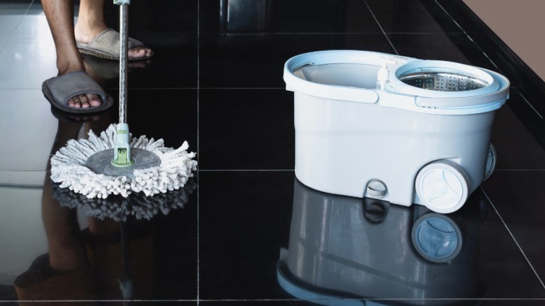 Sandalet içinde bir adam siyah banyo zeminde spin paspas kullanıyor