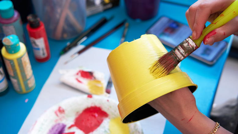 Bir kadın plastik bitki tenceresini parlak sarı boyar