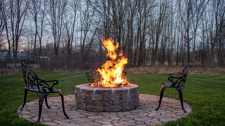 Akşam aydınlatmasında taş bir şöminenin ve veranda etrafında oturan üç şık demir sandalye.