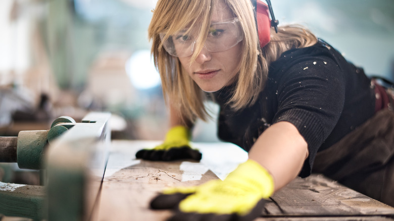 Bir masa testeresi ile tahta tahta kesen bir kadın.