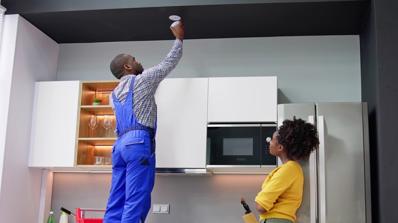 Handyman mutfakta duman alarmı kurarken ev sahibi izliyor