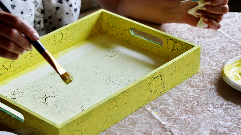 Bir kadın ahşap bir tepsi sarı boyuyor.