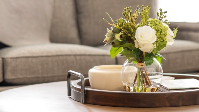 Cam vazo ve beyaz kase, yuvarlak sehpa üzerinde dairesel tepsiye oturan beyaz kase