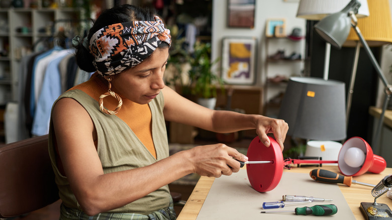 Bir kadın vidaları eski bir kırmızı lambanın tabanından çıkarır