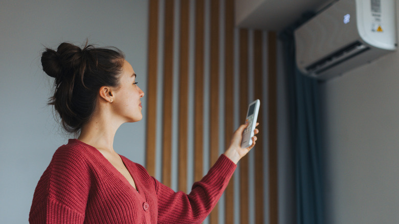 Bir kadın, duvara monte bir klima ünitesini ayarlamak için uzaktan kumanda kullanır