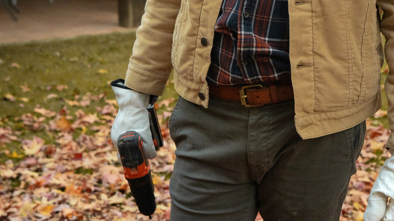 Kablosuz bir matkapla arka bahçede duran bir adam