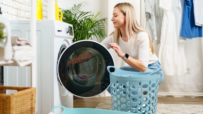 Beyaz çamaşır makinesinden çamaşır giyen kadın mavi sepete