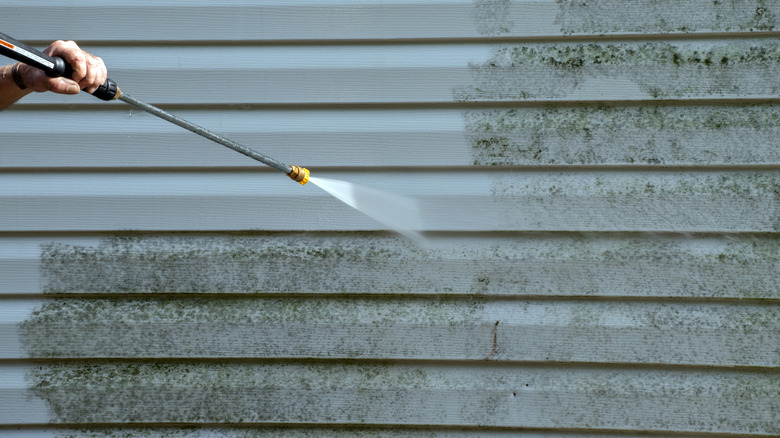 Basınçlı bir yıkama ile vinil sidingden kalıp ve küf temizleyen bir kişi