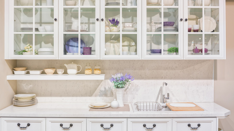 Şık mutfakta mor ve beyaz seramik tabakları olan basit beyaz ve cam dolaplar