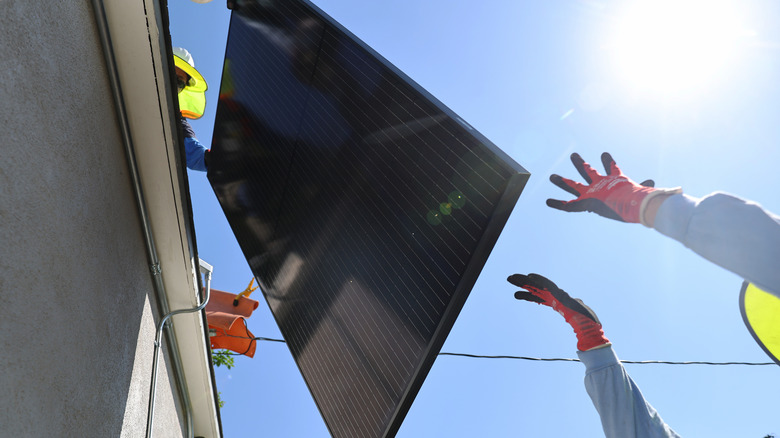 Büyük bir güneş paneli, bir evin çatısından yerdeki bir kişinin uzanmış kollarına indirilir