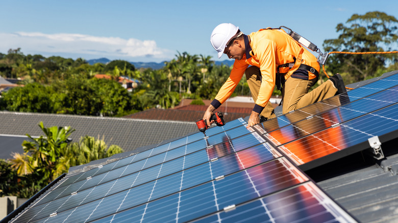 Bir montajcı, bir çatı üzerine güneş panellerini monte etmek için bir matkap kullanır