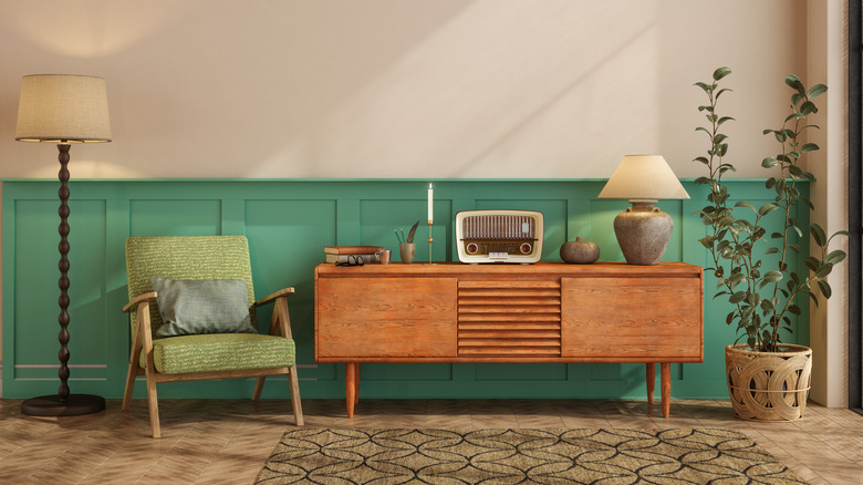 Yeşil bir koltuk, ayakta lambanın yanında, üstte vintage radyo, lamba, kitap ve mum içeren ahşap konsol masası