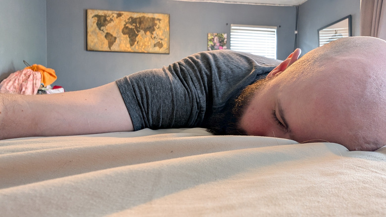 Kalak adam, krem ​​rengi çarşaflarla rahat yatak üzerinde yüz yüze yatıyor