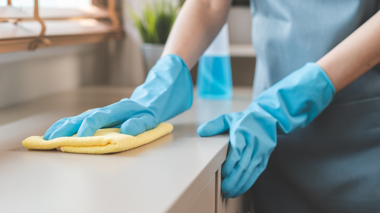 Mavi kauçuk eldivenlerde eller, bir tezgahı silmek için açık sarı bir mikrofiber havlu kullanır